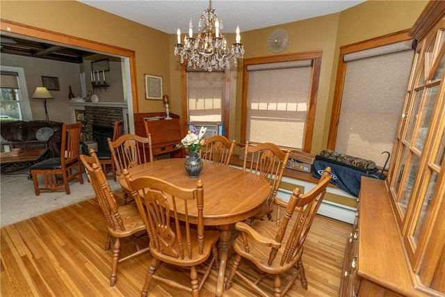 dining space with healthy amount of natural light, a chandelier, a fireplace, and light wood-style flooring