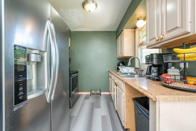 102 Wall Ave, Des Moines, IA 50315 - kitchen with appliances with stainless steel finishes, a sink, light countertops, wood finished floors, and a textured ceiling