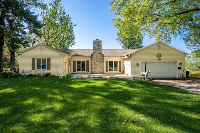 back of house with a garage, driveway, a chimney, and a lawn