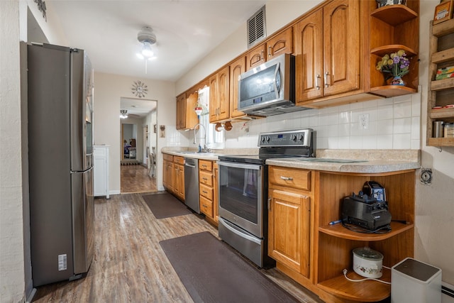 kitchen featuring appliances with stainless steel finishes, open shelves, light countertops, a sink, and wood finished floors
