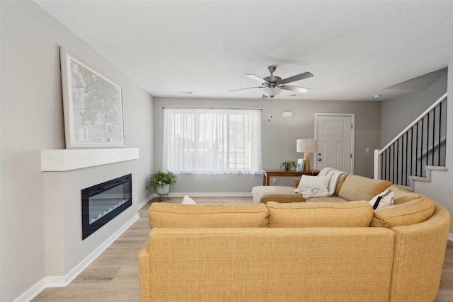 2642 SE Osier Ave, West Des Moines, IA 50265 - living room featuring light wood-style floors, a ceiling fan, a glass covered fireplace, and stairway
