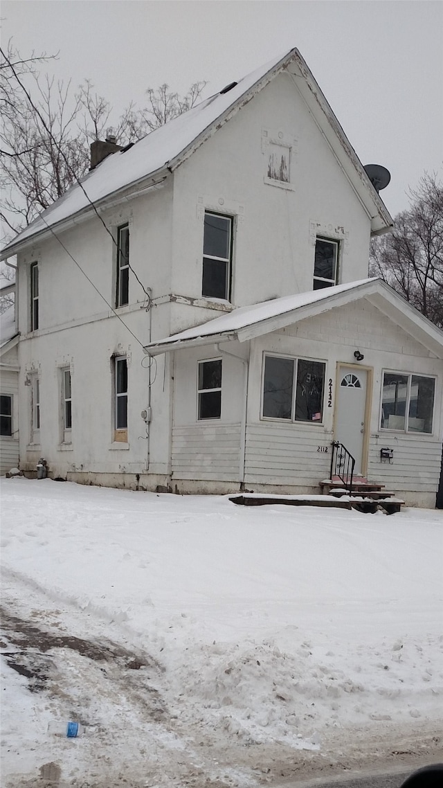 snow covered back of property with a chimney and stucco siding