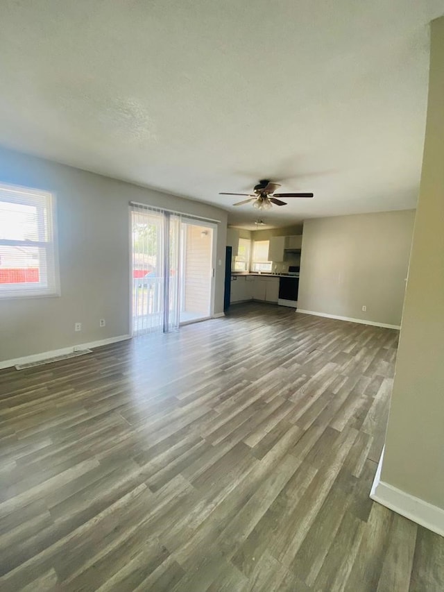 unfurnished living room with baseboards, a ceiling fan, and dark wood finished floors