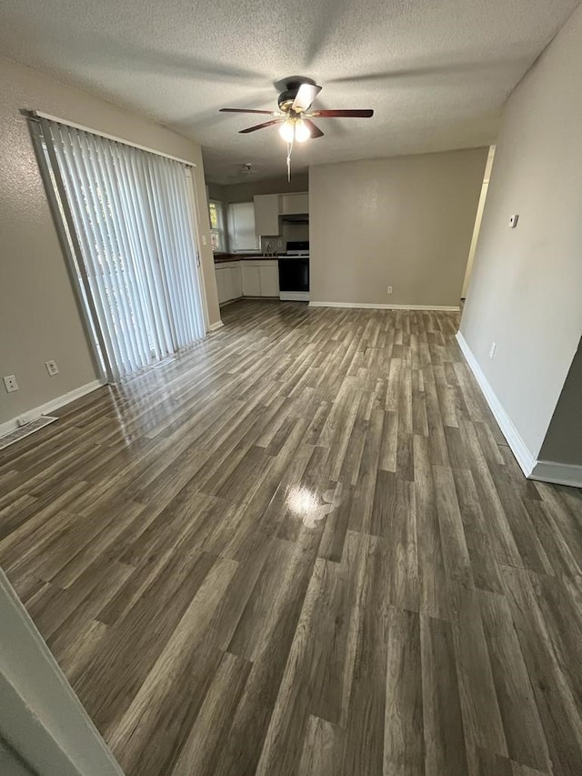 unfurnished living room featuring a ceiling fan, dark wood finished floors, baseboards, and a textured ceiling