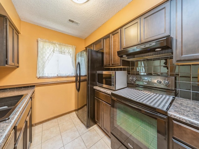 5200 Twana Dr, Des Moines, IA 50310 - kitchen featuring black range with electric stovetop, under cabinet range hood, stainless steel microwave, freestanding refrigerator, and decorative backsplash