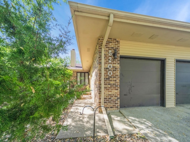 5200 Twana Dr, Des Moines, IA 50310 - view of exterior entry featuring brick siding, a garage, and gravel driveway