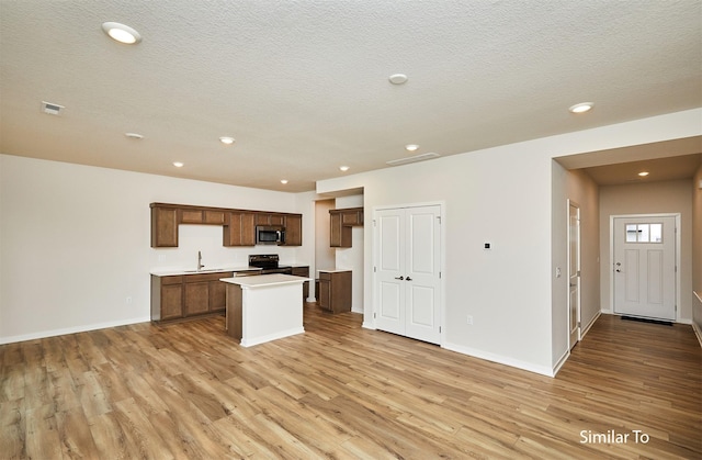 kitchen featuring stainless steel microwave, black range with electric cooktop, light wood-style flooring, a kitchen island, and recessed lighting