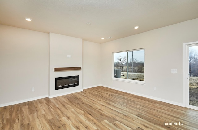 unfurnished living room with light wood-style flooring, a glass covered fireplace, healthy amount of natural light, and recessed lighting