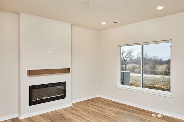 unfurnished living room featuring a glass covered fireplace, light wood-style floors, baseboards, and recessed lighting