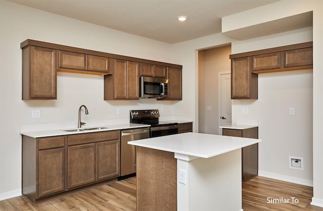 kitchen with stainless steel appliances, a sink, light wood finished floors, baseboards, and light countertops