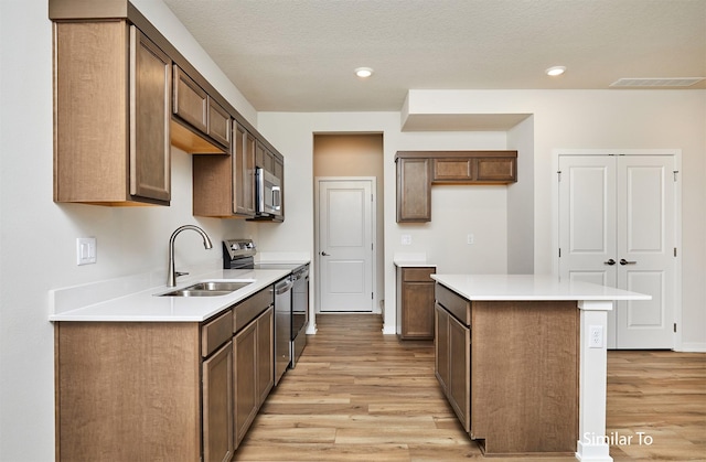 kitchen featuring a sink, stainless steel appliances, light wood-type flooring, a center island, and light countertops