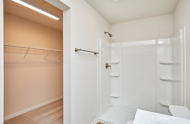 bathroom featuring a shower, toilet, a spacious closet, and baseboards