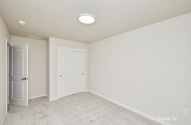 unfurnished bedroom with light carpet, baseboards, a closet, and a textured ceiling