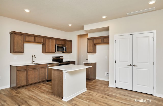 kitchen with stainless steel appliances, a sink, light wood finished floors, light countertops, and a kitchen island