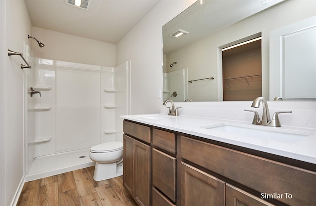 bathroom with wood finished floors, toilet, a shower, and double vanity