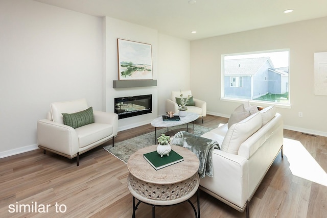 living area featuring a glass covered fireplace, light wood-style floors, baseboards, and recessed lighting