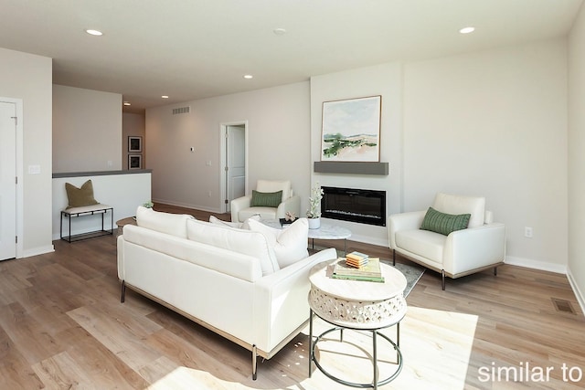 living area with light wood finished floors, recessed lighting, baseboards, and a glass covered fireplace