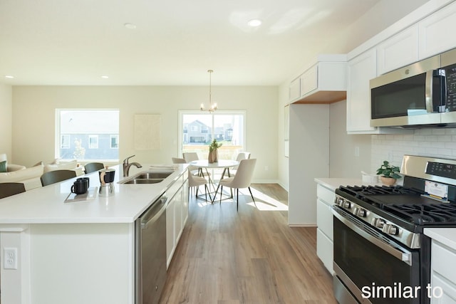 kitchen with stainless steel appliances, a sink, light wood-style flooring, white cabinetry, and a chandelier