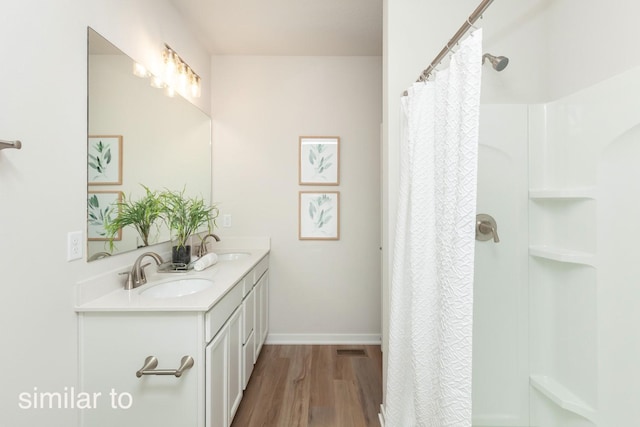 bathroom featuring wood finished floors, a shower with shower curtain, double vanity, and baseboards