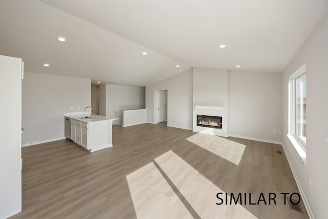6565 NE 11th Ct, Des Moines, IA 50313 - unfurnished living room featuring a sink, light wood-style floors, vaulted ceiling, baseboards, and a glass covered fireplace