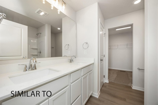 6557 NE 11th Ct, Des Moines, IA 50313 - bathroom with double vanity, wood finished floors, a walk in closet, a shower, and recessed lighting