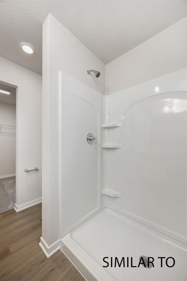 6557 NE 11th Ct, Des Moines, IA 50313 - full bathroom featuring a walk in shower, a textured ceiling, wood finished floors, and a walk in closet