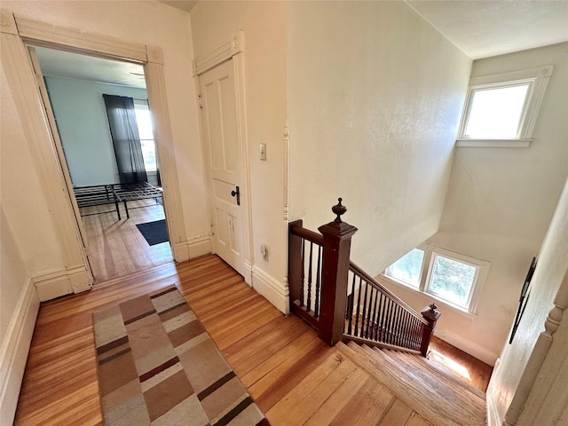 hall with light wood-style floors, an upstairs landing, healthy amount of natural light, and baseboards