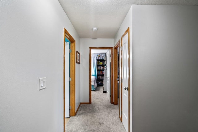 hall with light carpet, baseboards, and a textured ceiling