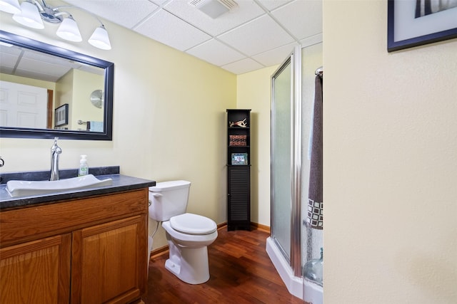 bathroom with a drop ceiling, wood finished floors, a stall shower, toilet, and vanity