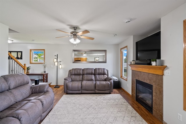 living area with a tile fireplace, wood finished floors, a ceiling fan, and stairway