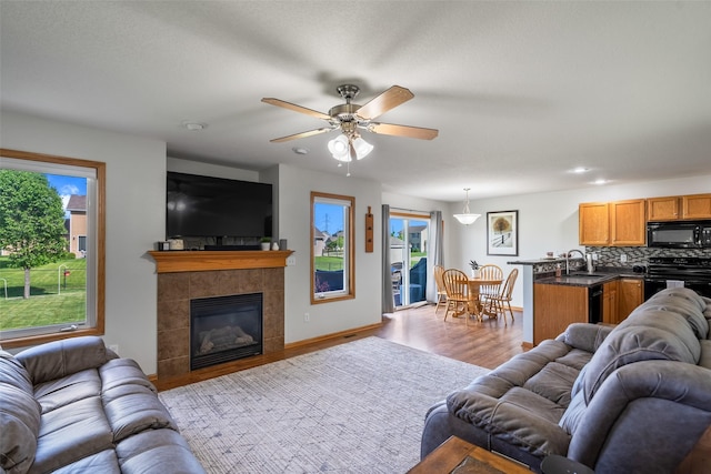 living room with plenty of natural light, wood finished floors, a ceiling fan, a tiled fireplace, and recessed lighting