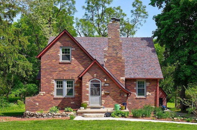 tudor house featuring a chimney, brick siding, and a front lawn