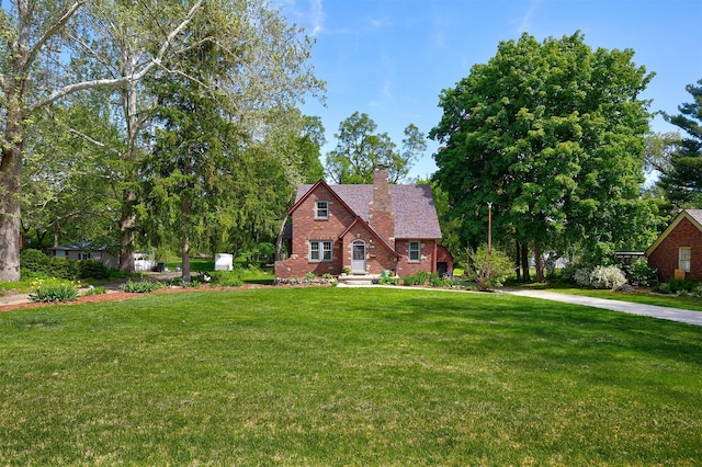 tudor house with a chimney, a front lawn, and brick siding