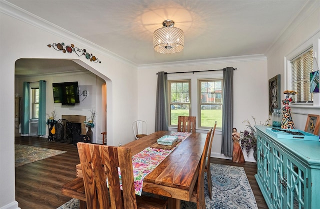dining room featuring arched walkways, wood finished floors, a chandelier, crown molding, and a fireplace