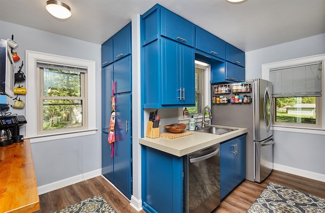 kitchen featuring a sink, appliances with stainless steel finishes, blue cabinetry, and dark wood-style floors