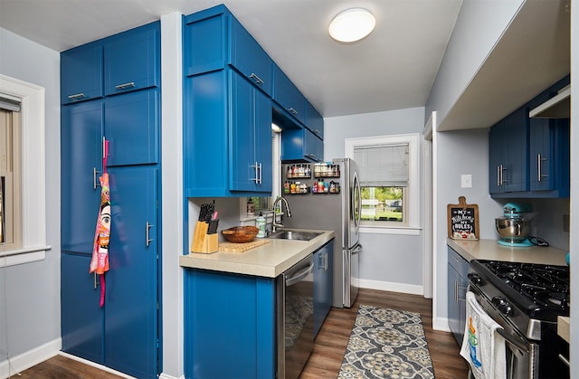 kitchen with stainless steel appliances, blue cabinetry, light countertops, and dark wood-style floors
