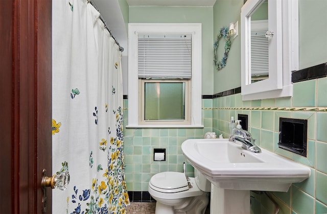 full bathroom with tile walls, toilet, a shower with curtain, wainscoting, and tile patterned floors