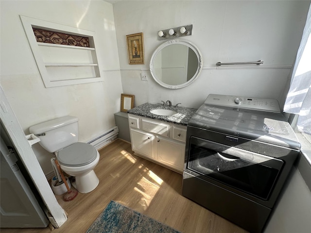 bathroom with washer / clothes dryer, a baseboard heating unit, wood finished floors, toilet, and vanity