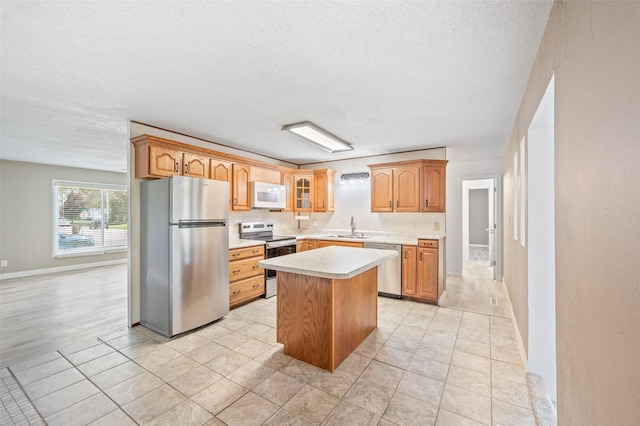 kitchen featuring stainless steel appliances, a sink, light countertops, a textured ceiling, and a kitchen island