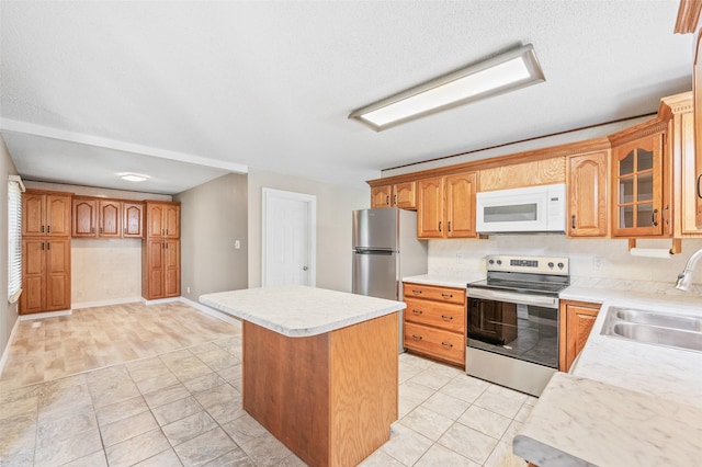 kitchen featuring stainless steel appliances, a sink, light countertops, glass insert cabinets, and a center island