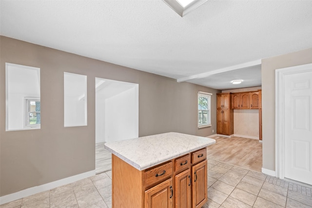 kitchen with light countertops, baseboards, a kitchen island, light tile patterned flooring, and a textured ceiling