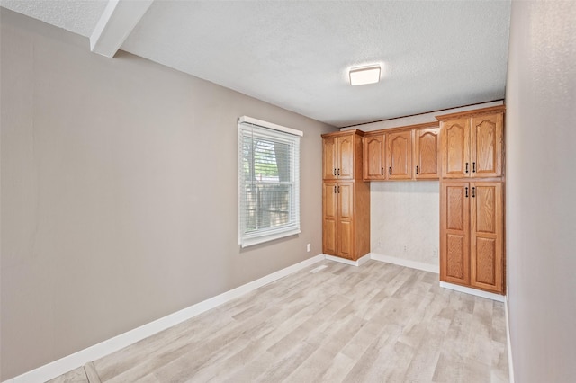 unfurnished room with a textured ceiling, light wood finished floors, baseboards, and beam ceiling