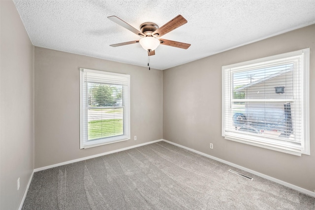 empty room featuring healthy amount of natural light, ceiling fan, carpet floors, baseboards, and a textured ceiling