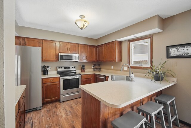 7052 Plum Dr, Urbandale, IA 50322 - kitchen featuring appliances with stainless steel finishes, a sink, a peninsula, a breakfast bar, and light countertops