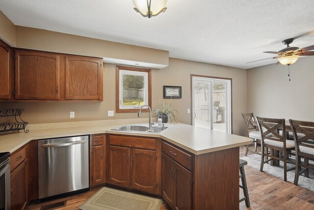 7052 Plum Dr, Urbandale, IA 50322 - kitchen featuring stainless steel dishwasher, a sink, a peninsula, light wood-type flooring, and a textured ceiling
