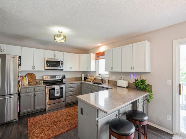 5031 Cherrywood Dr, West Des Moines, IA 50265 - kitchen featuring stainless steel appliances, a peninsula, dark wood-style floors, a kitchen bar, and white cabinets
