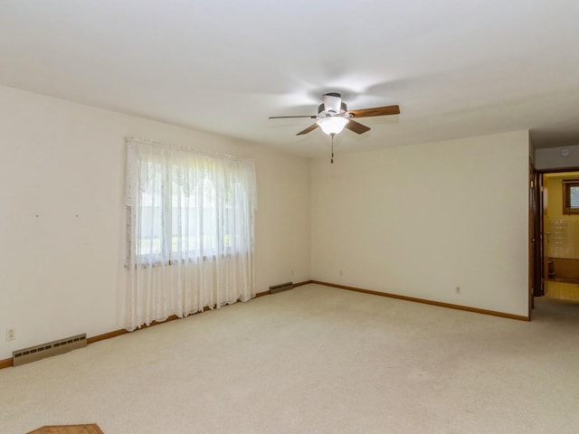 empty room featuring a ceiling fan, plenty of natural light, baseboard heating, and light carpet