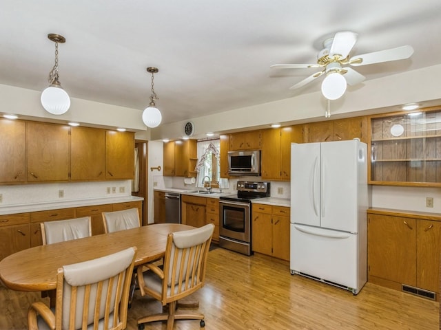 kitchen featuring appliances with stainless steel finishes, a sink, brown cabinets, light countertops, and decorative light fixtures