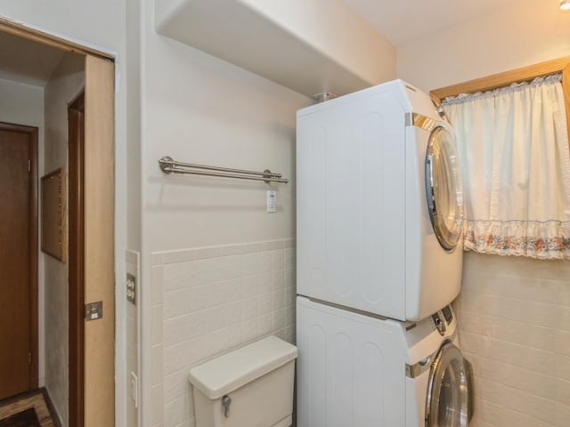 bathroom with estacked washer and dryer, tile walls, toilet, and wainscoting