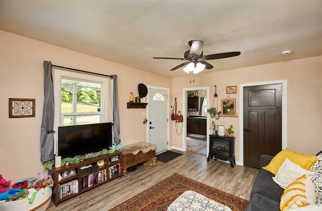 living room with a wood stove, wood finished floors, ceiling fan, and baseboards